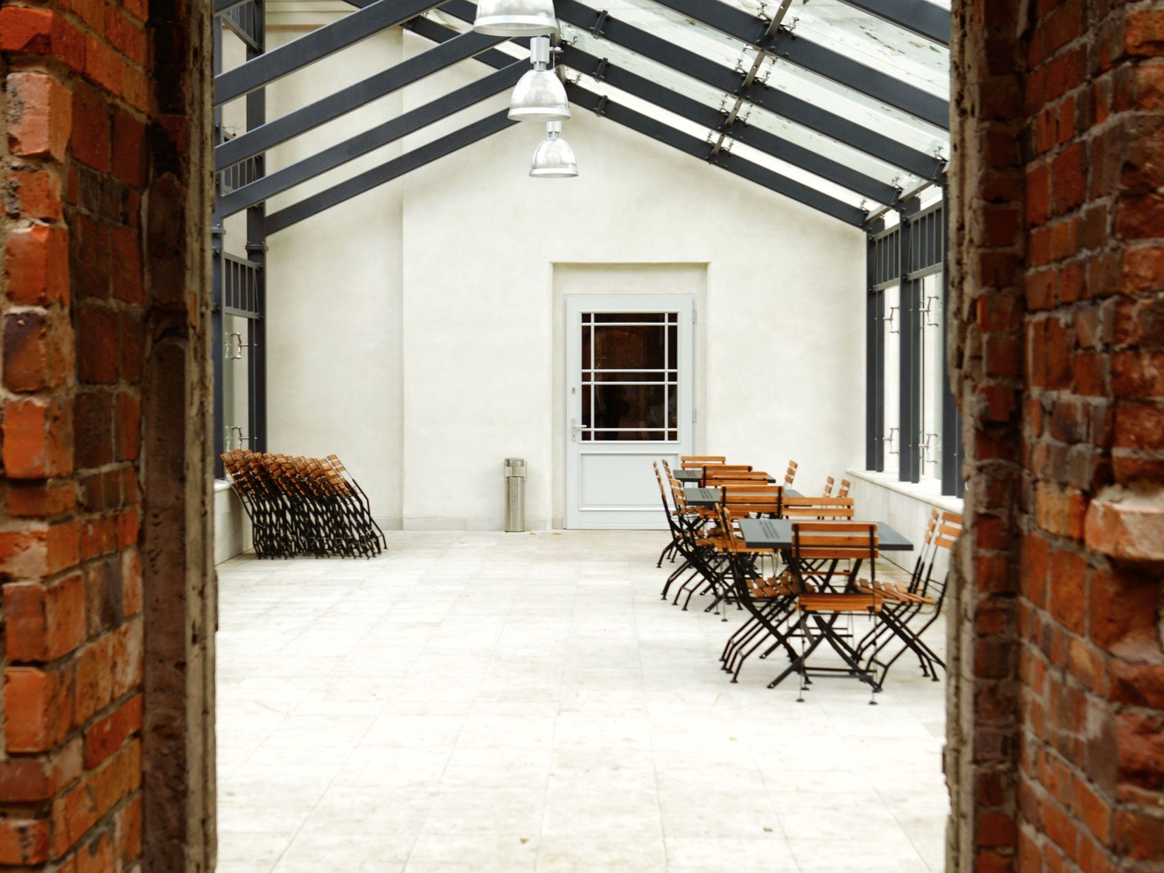 Indoor dining area with wooden tables and chairs under a glass roof.