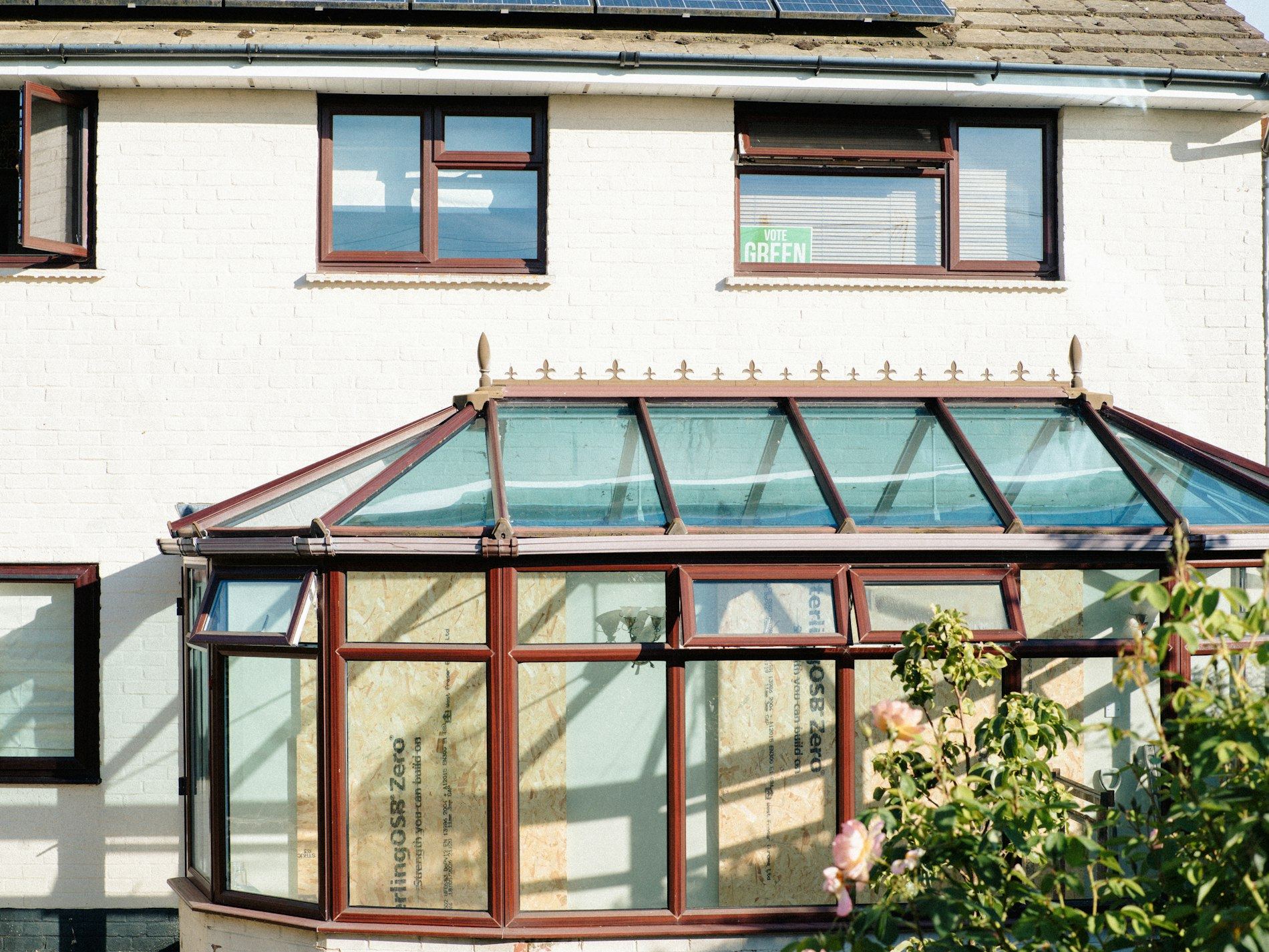 White semi-detached house with a brown-framed conservatory on the side.