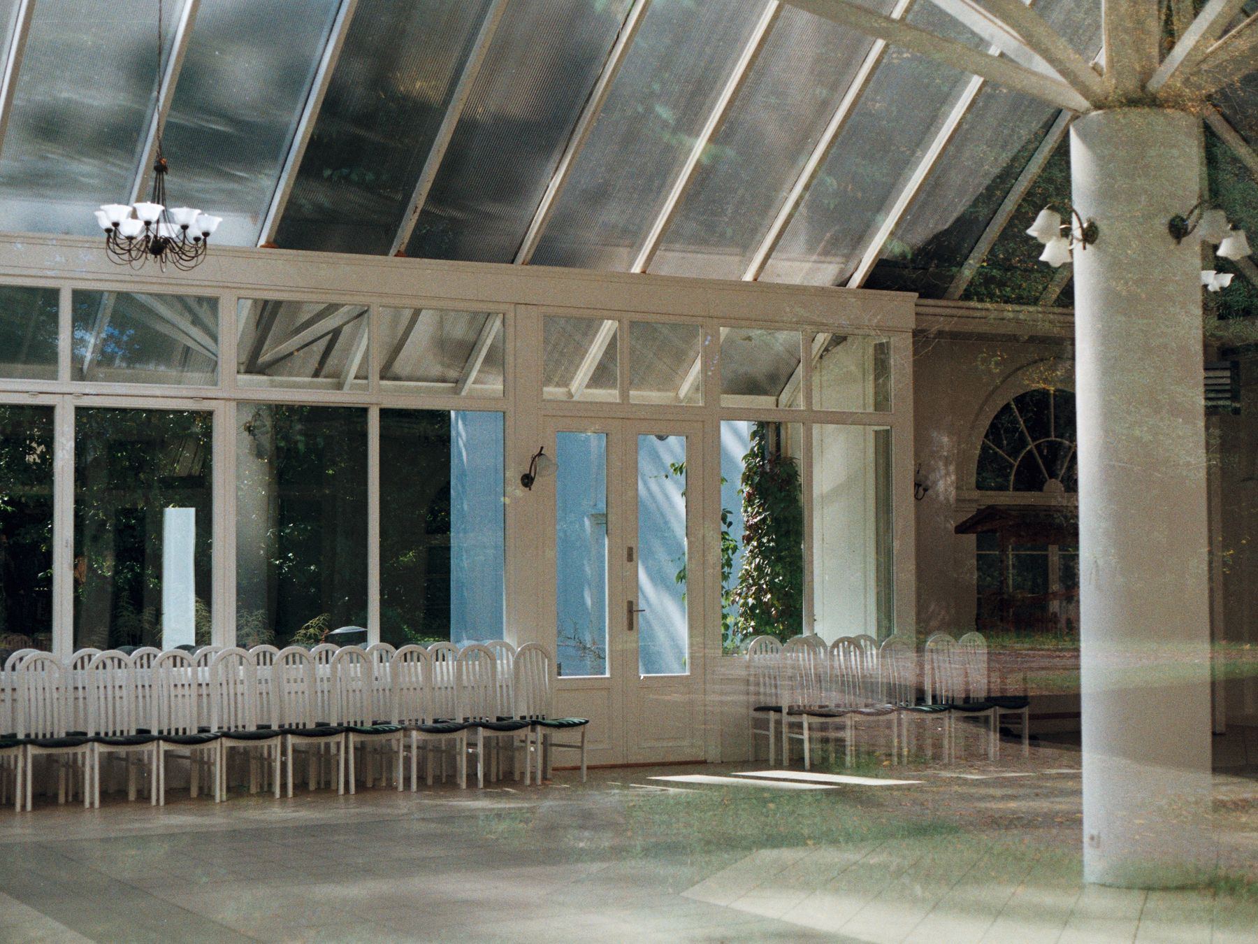 Blurred, double-exposed conservatory interior with rows of white chairs.